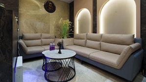 A modern living room with a beige sectional sofa, a round coffee table, and a decorative vase. - Hotel Hari Om (Dwarka)
