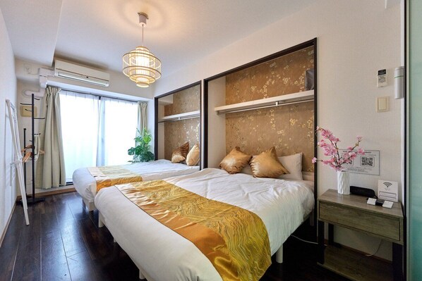 A hotel room with two beds, a large window, an air conditioning unit, a bedside table with a vase of flowers, and a wall-mounted shelf. - XS54 (XS08,XS49) XROSS STAY Namba23 (大阪市中央区島之内)