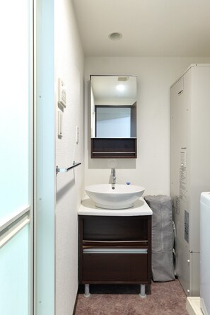 A compact bathroom with a white sink, dark wooden vanity, a mirror above the sink, and a towel rack. - XS54 (XS08,XS49) XROSS STAY Namba23 (大阪市中央区島之内)