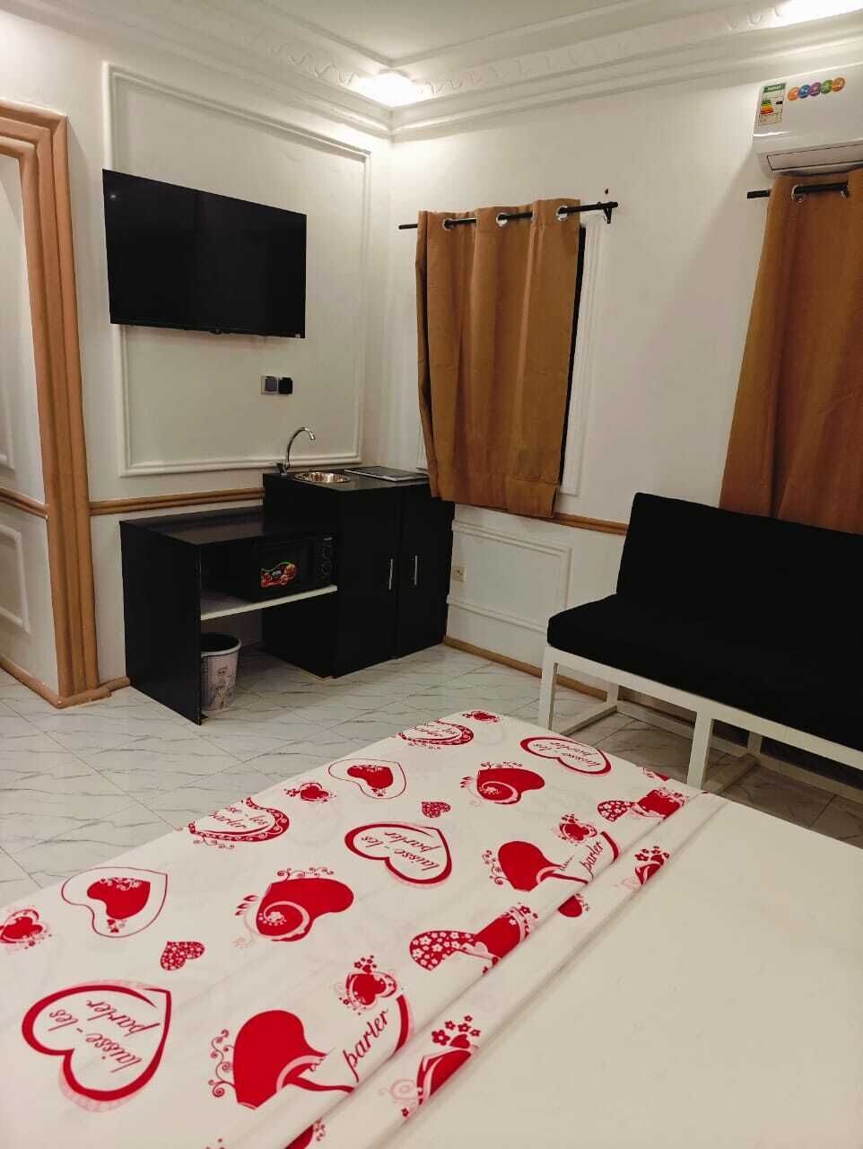 A room with a television, a small kitchenette, a black chair, and a patterned tablecloth.