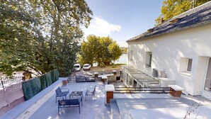Eine Dachterrasse mit Gartenmöbeln, ein weißes Gebäude und Bäume.