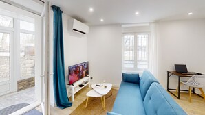Ein modernes Wohnzimmer mit einem blauen Sofa, einem Fernseher, einem Laptop auf einem Schreibtisch und einem großen Fenster.