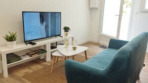 A living room with a television, a small table with a bottle and glasses, a blue sofa, and a potted plant. - Apartment 'Cosy Calme Bord De Seine Jardin' with Wi-Fi (Le Mée-sur-Seine)