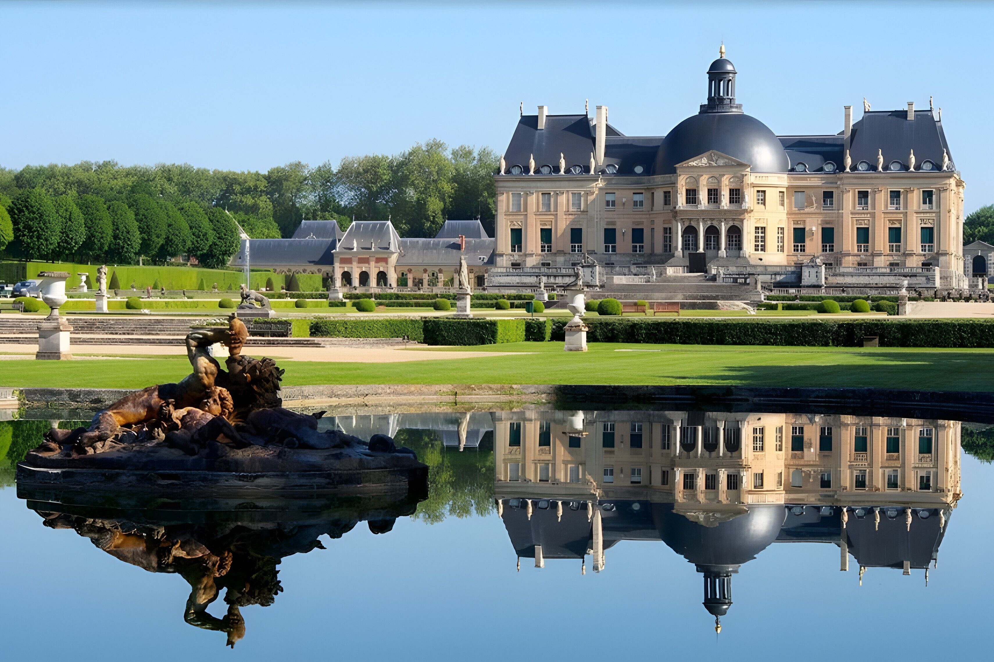 A grand palace with a symmetrical garden and a central fountain reflecting the building.