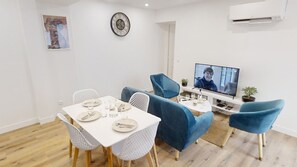 Un salon moderne comprenant un coin repas, un téléviseur à écran plat et une horloge murale.