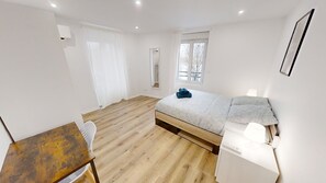 Une chambre à coucher avec un lit, un bureau, une chaise, une fenêtre et un miroir.