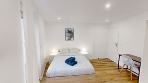 A bedroom with a bed, bedside lamps, a desk with a chair, and a wall-mounted artwork. - Apartment 'Cosy Calm Seine Riverside Garden' with Balcony and Wi-Fi (Le Mée-sur-Seine)
