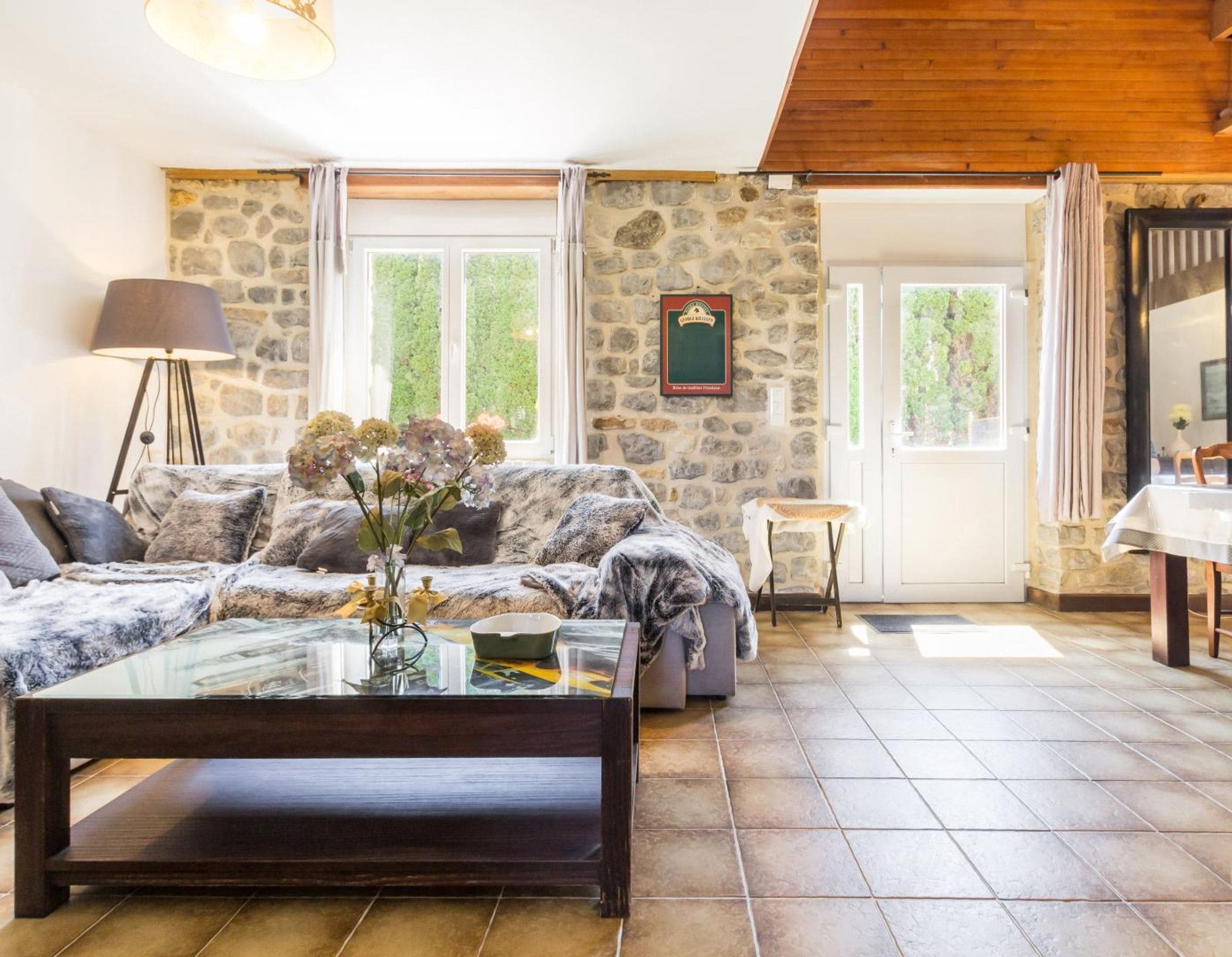 Una sala de estar acogedora con pared de piedra, sofá, mesa de centro y lámpara.