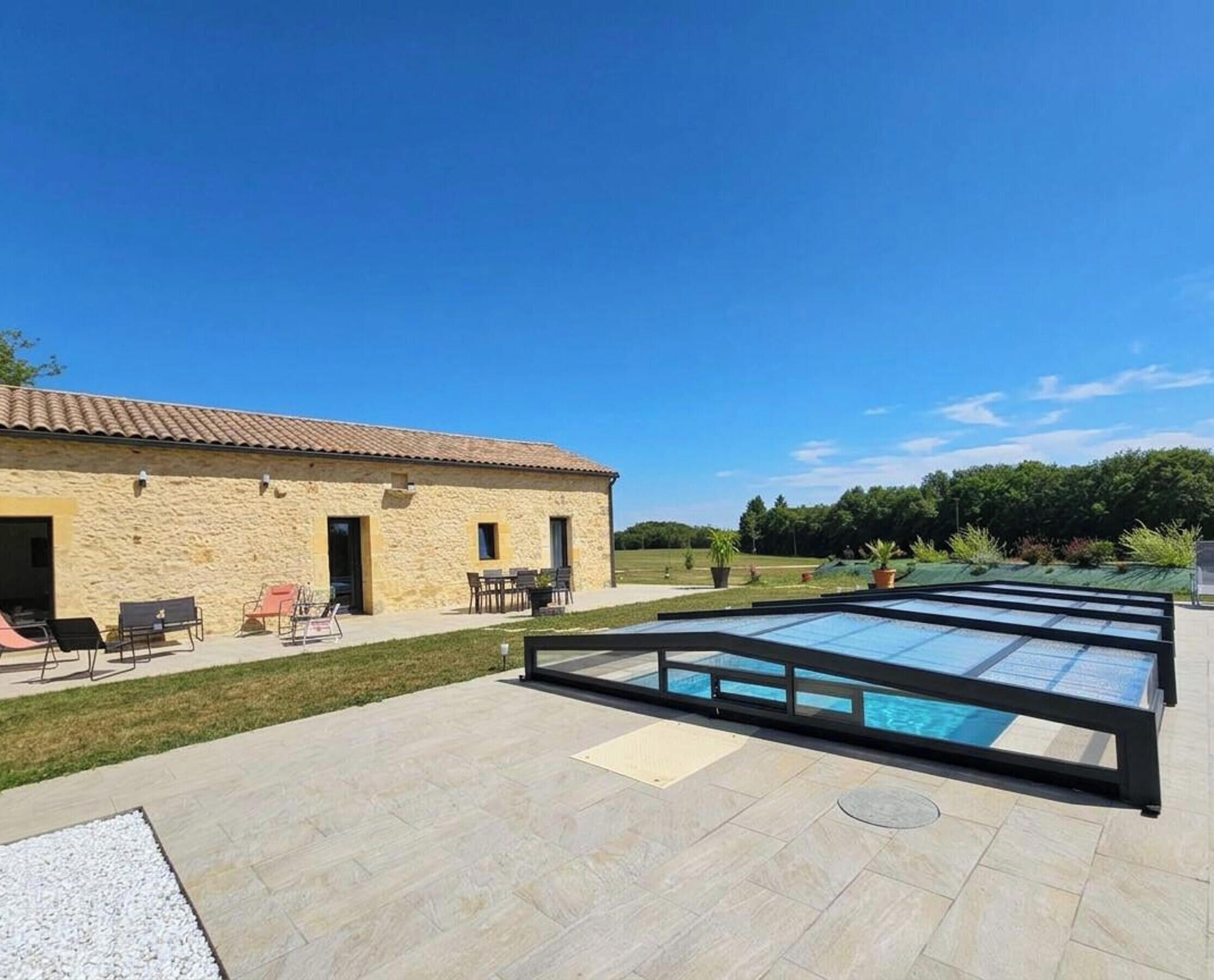 A stone building with a pool area, outdoor seating, and a clear sky.