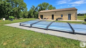 Un bâtiment en pierre avec un toit en tuiles, une piscine et une pelouse.