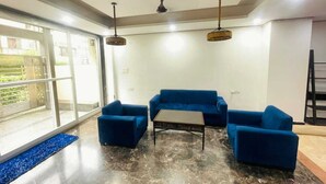 Une pièce dotée d’une grande porte-fenêtre coulissante, d’un canapé bleu, d’une petite table et d’un ventilateur de plafond.