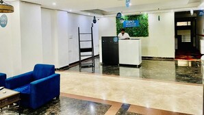 Un espace d’accueil comprenant un comptoir de réception, un canapé bleu, une échelle et un élément de décoration murale vert.