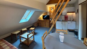 Een compacte, goed verlichte kamer met een vide, een eettafel en een keuken met houten kastjes en een inbouwoven.