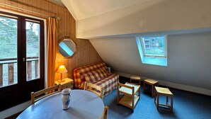 Een gezellig slaapkamer op zolder met houten balkenplafond, een geruit bankje, een klein tafeltje en een raam met uitzicht op de omgeving.