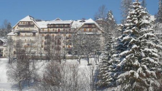 A large, multi-story hotel with a traditional architectural style, surrounded by snow-covered trees and a clear blue sky.