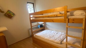 A bunk bed room with wooden frames, white bedding, and a small window.