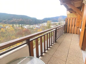 A balcony with a wooden railing, a glass table, and a view of a town and mountains.