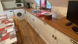 A compact kitchen with a microwave, washing machine, sink, and a dining area with a table.