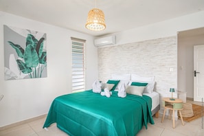 Une chambre à coucher comprenant un lit, un luminaire suspendu, une fenêtre avec des stores et un climatiseur fixé au mur.
