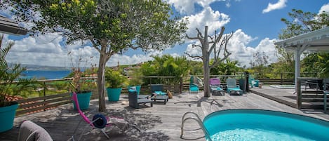 A wooden deck with a pool, lounge chairs, and potted plants.