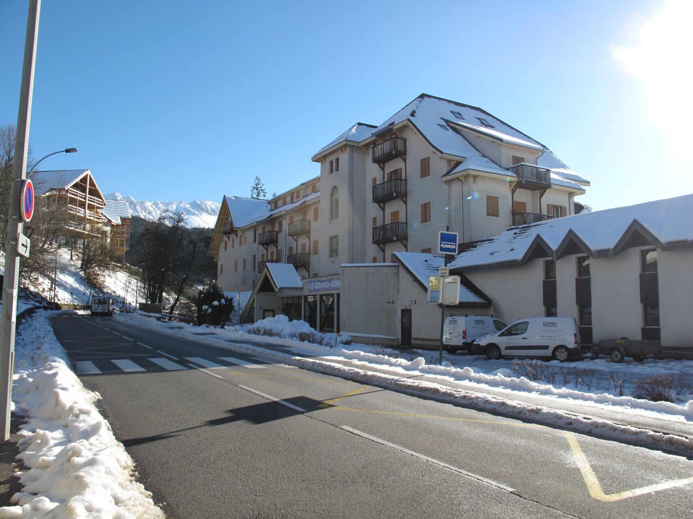 A snow-covered street with a hotel named "Le Grand Adr" and a building with balconies.
