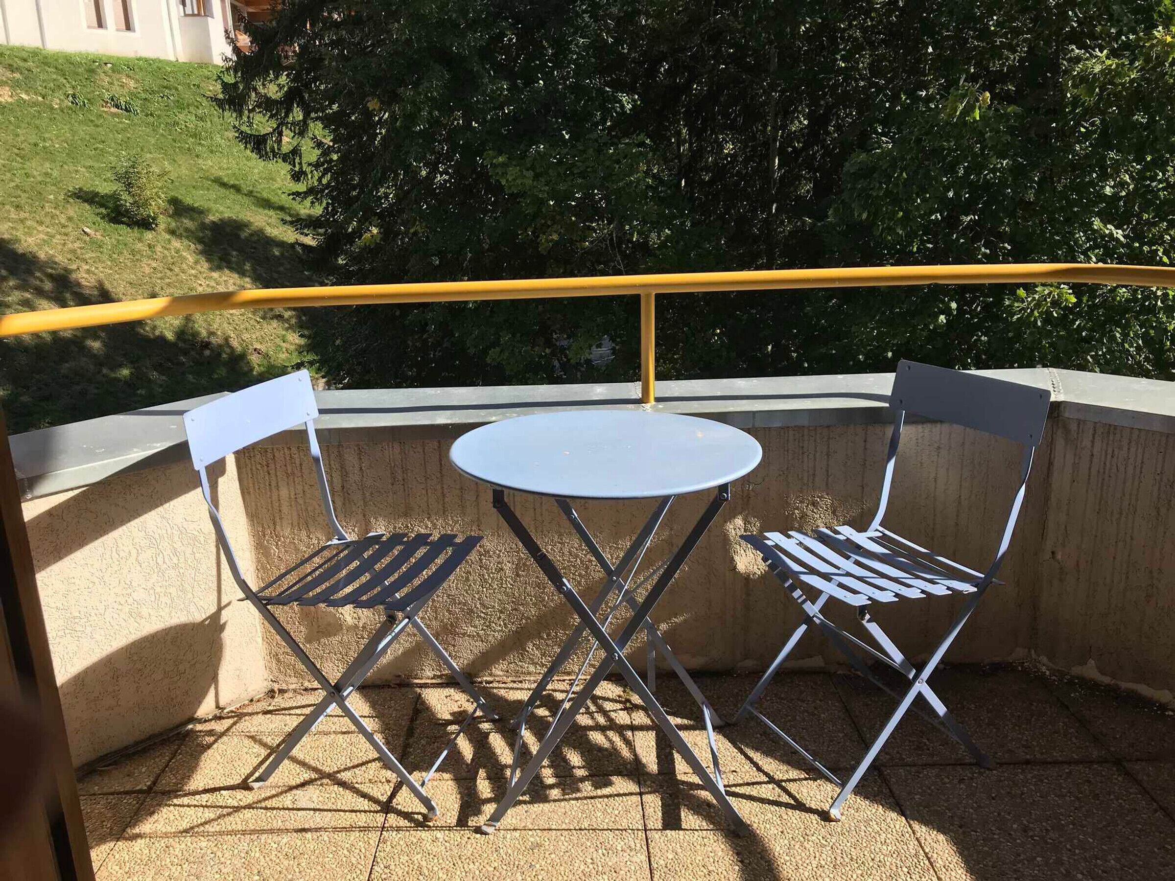 Een klein balkon buiten met een ronde tafel en twee metalen stoelen.