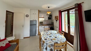 A compact kitchen with a refrigerator, microwave, and sink. A dining table with chairs is positioned near a window with curtains. - 2-room apartment with balcony and mountain views (Villard-de-Lans)