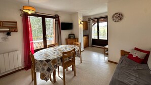 A cozy room with a dining table, chairs, a bed, a TV, and a kitchen area. - 2-room apartment with balcony and mountain views (Villard-de-Lans)