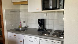 A compact kitchen with white cabinets, a Bosch dishwasher, a coffee maker, a microwave, and a gas stove. - Cozy apartment with balcony and park view in Villard-de-Lans (Villard-de-Lans)