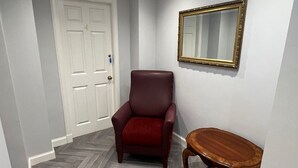 A hallway with a red leather chair, a wooden side table, a white door, and a mirror on the wall. - Mayfield Suites  (Edinburgh)