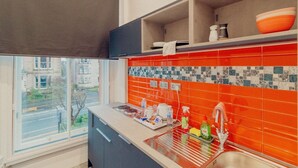 A modern kitchen with a large window, orange tiled backsplash, and a variety of kitchen items on the counter. - Mayfield Suites  (Edinburgh)