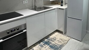 A modern kitchen with white cabinetry, a stainless steel sink, a built-in oven, and a refrigerator. - Portu Sereno Emerald - Floor 1 (Setúbal)