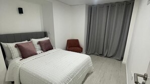 A modern bedroom with a large bed, a chair, and a view of the outside through a window with curtains. - Portu Sereno Emerald - Floor 1 (Setúbal)