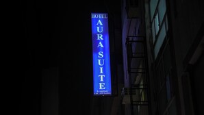 Ein Hotel namens 'Hotel Aura Suite' mit auffälliger Schilderung, umgeben von weiteren Gebäuden und Schildern.