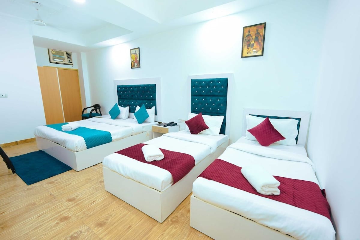 Quarto de hotel com três camas, piso de madeira, um guarda-roupa e um quadro na parede.