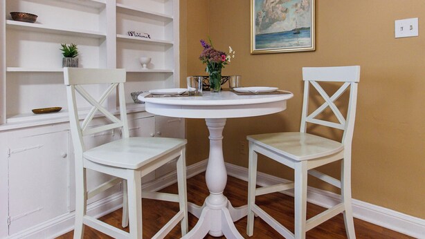 A dining area with a white round table and two white chairs, surrounded by white shelves with various items. - Comfy 1 BR Hide Away Apt w/ Garage Parking (Bryn Mawr)