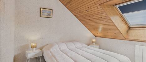 A bedroom with a sloped ceiling, a skylight, a bed with white bedding, and a bedside table with a lamp.