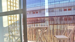Een balkon met een houten tafel en twee stoelen, een bamboe hek en uitzicht op een gebouw met ramen.