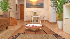 Een eetgedeelte met een ronde tafel, stoelen, een schaal eten en een potplant.