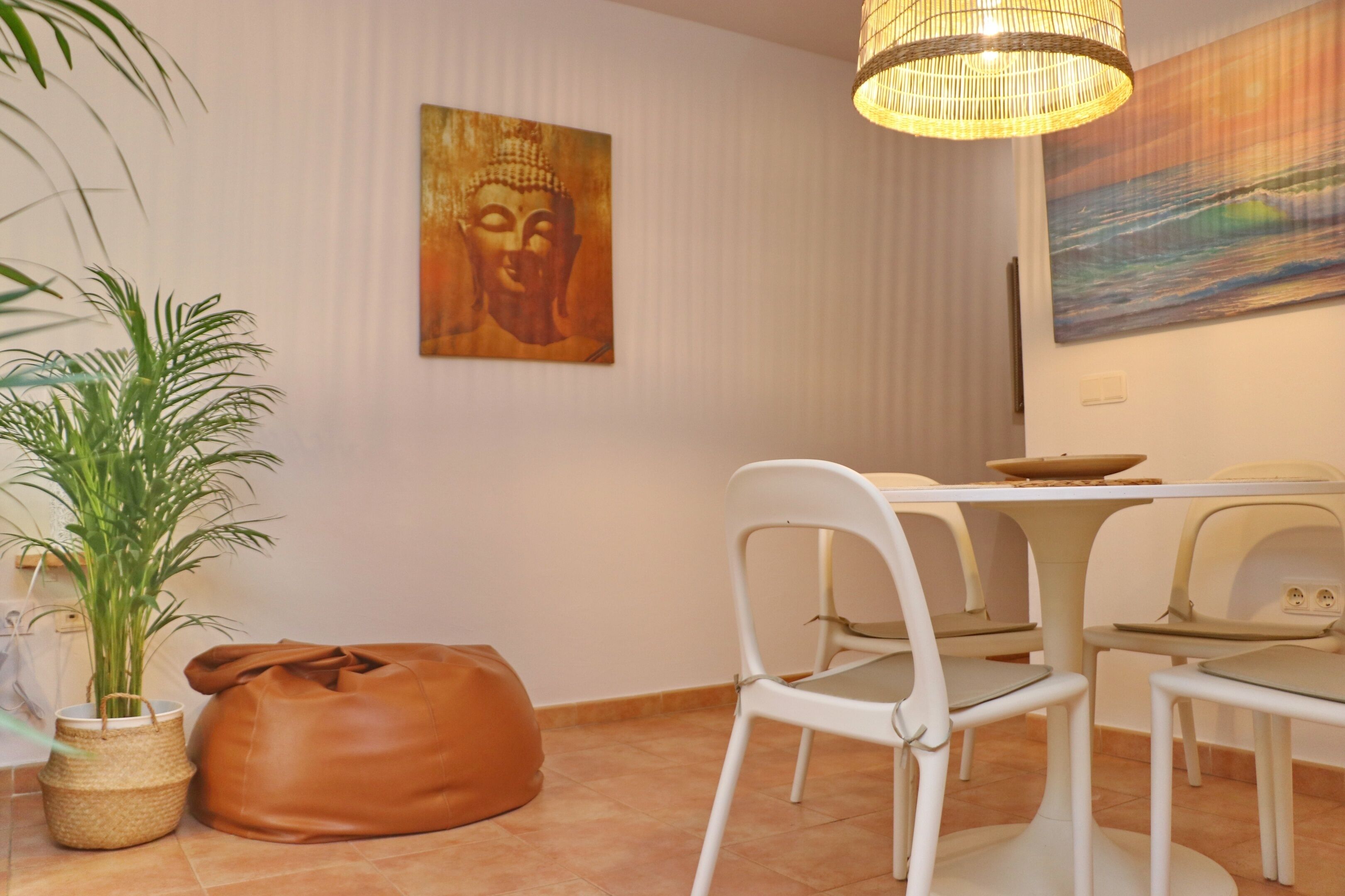 A dining area with a table, chairs, a Buddha painting, a potted plant, and a leather bag.