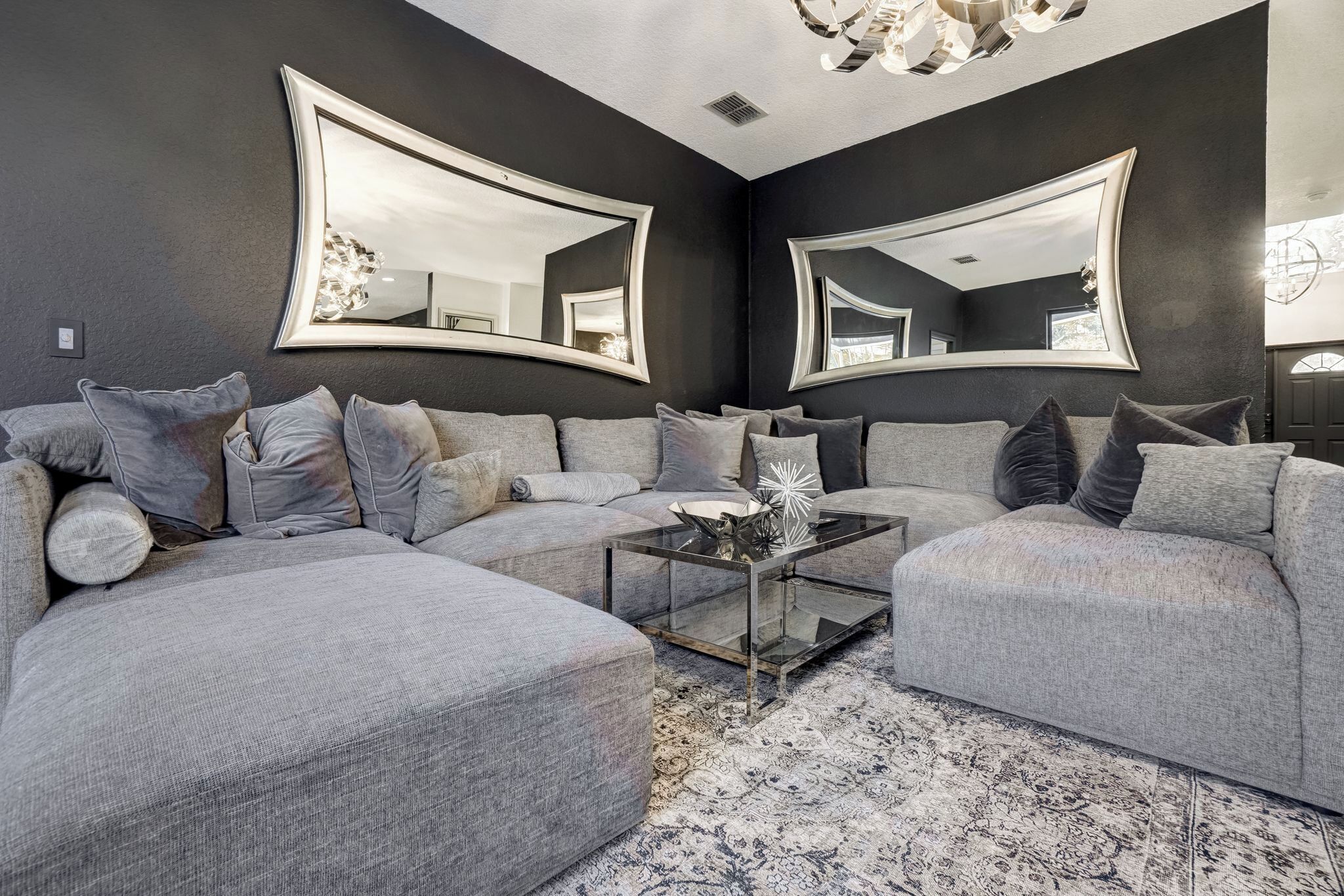 A modern living room with a sectional sofa, a glass coffee table, and two large mirrors on the walls.