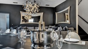 Un comedor moderno con una gran pieza central metálica, varios vasos de vino y un sofá al fondo.