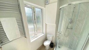 A bathroom with a toilet, a sink, a glass shower enclosure, and a window with frosted glass. - Cozy Croydon Apartment With Central Heating & Free Parking (Croydon)