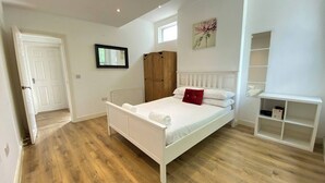 A bedroom with a white bed, wooden wardrobe, and a white shelf unit. - Cozy Croydon Apartment With Central Heating & Free Parking (Croydon)
