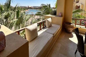 Ein Balkon mit einer Couch, einem Sessel und Blick auf einen Strand und Palmen.