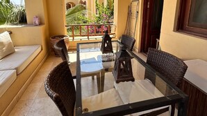 A sunlit patio with wicker furniture, a glass table, and a view of a garden.