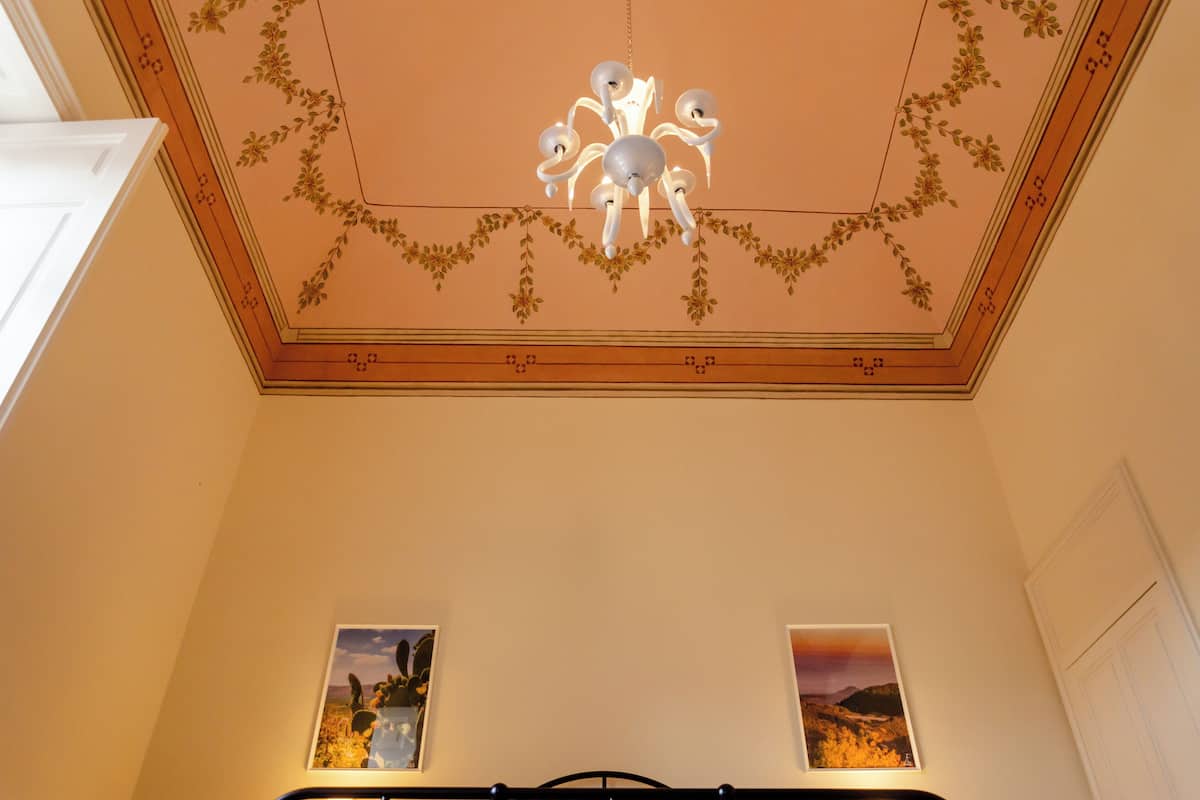 Una habitación con candelabro, diseño floral en el techo y dos cuadros en la pared.