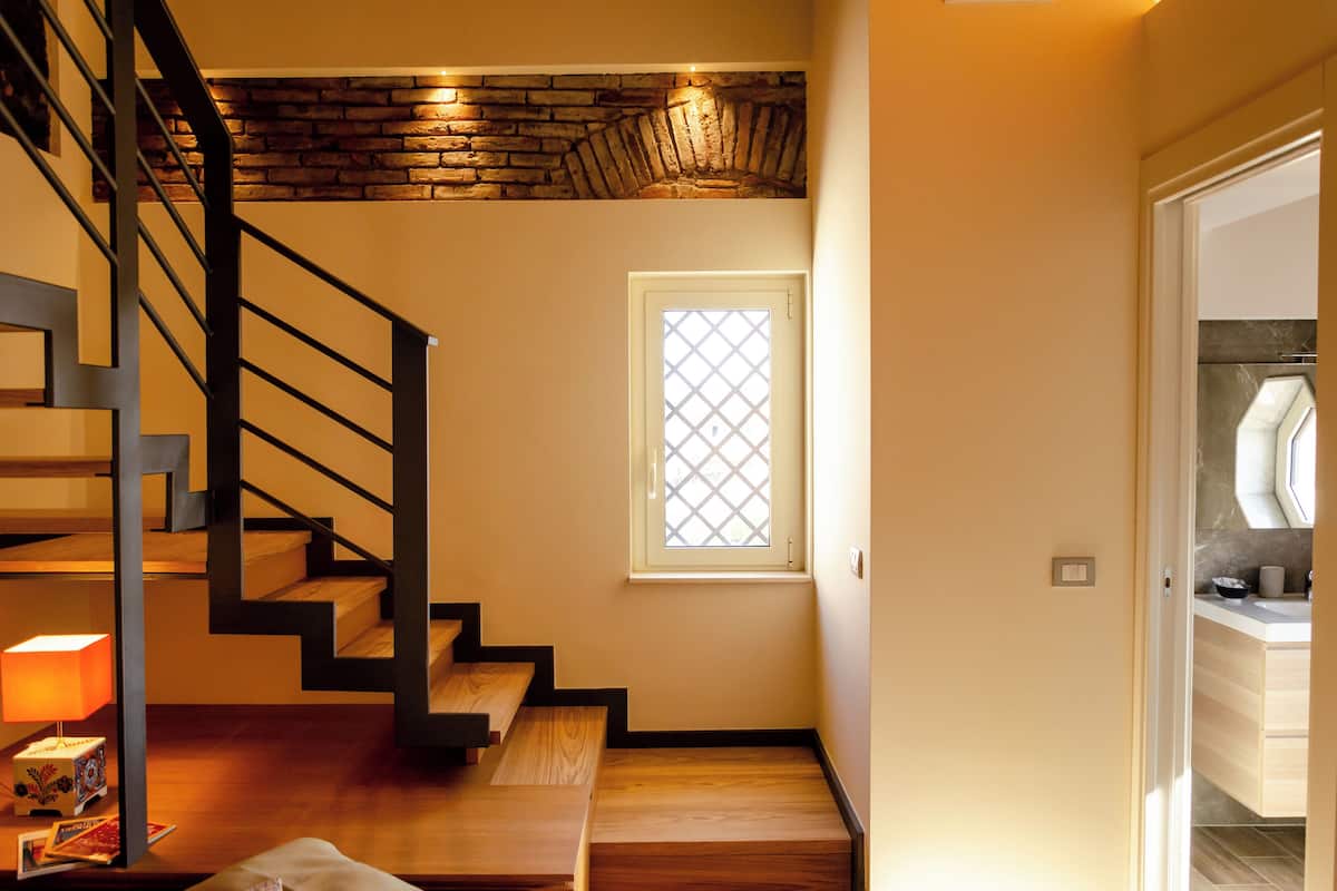 Una escalera con terminaciones de madera, un ventanal con diseño de celosía y una lámpara en el suelo.
