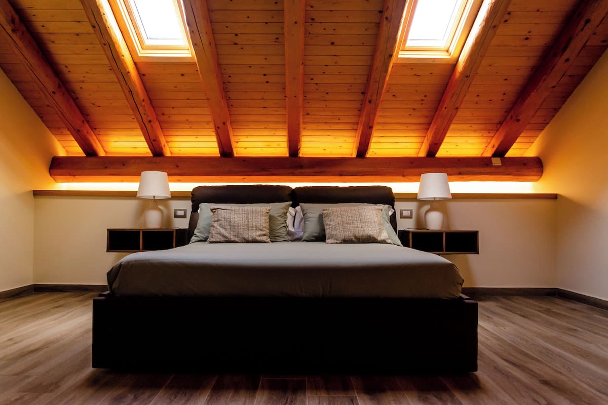 Un dormitorio con una cama grande, vigas de madera en el techo, tragaluces y lámparas de noche.