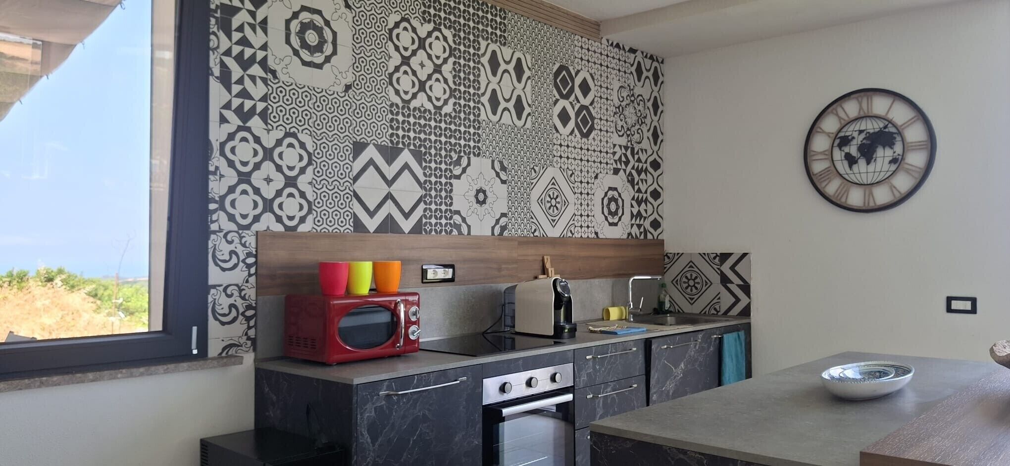 Una cocina moderna con salpicadero estampado, microondas, estufa y una zona de comedor con un bol sobre la mesa.